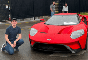 Young white man crouches next to a red sportscar